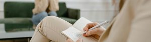 Une psychologue prend des notes dans un cahier en étant assise sur un canapé